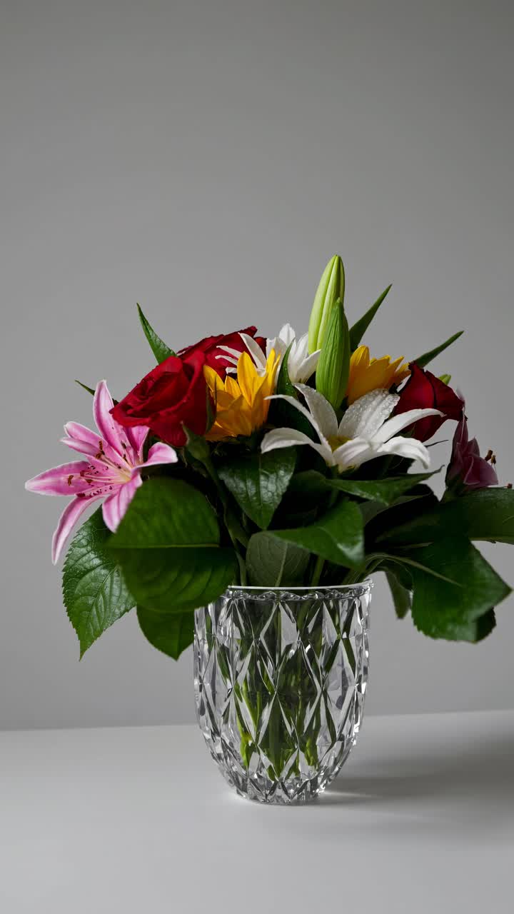 A close-up video of a vibrant floral arrangement in a crystal vase, captured from a side angle