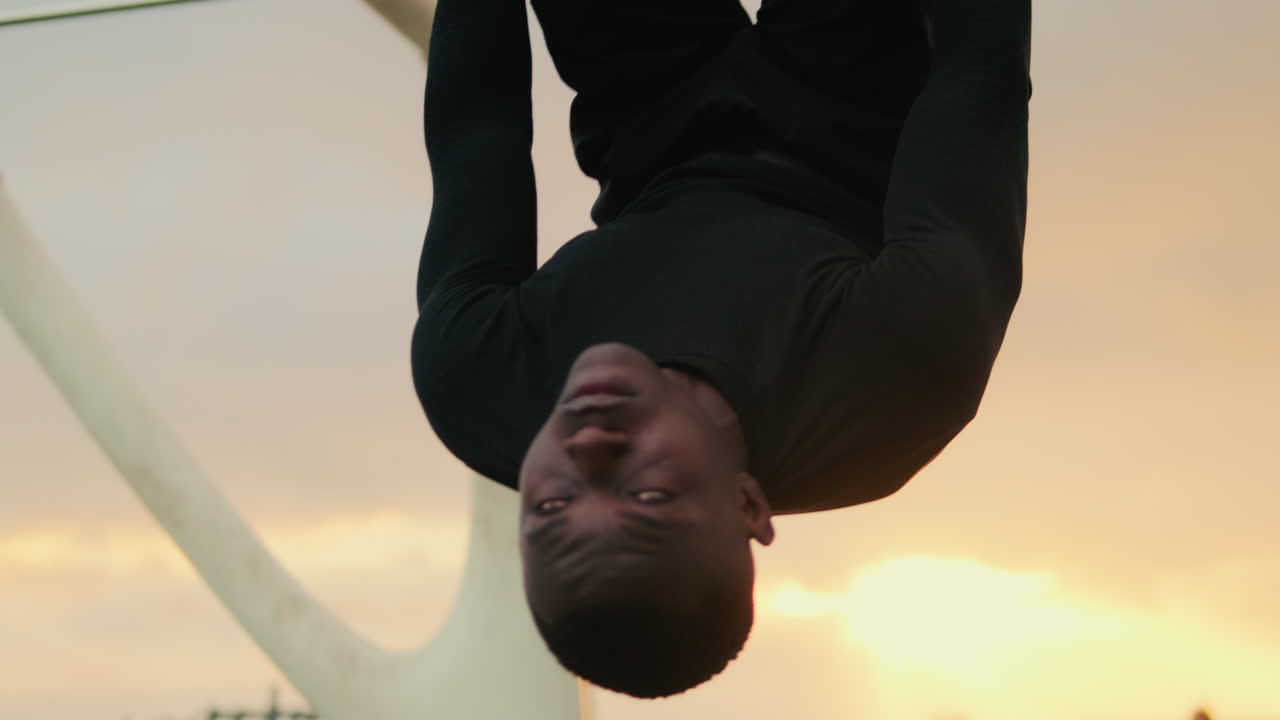 Homem Pendurado de Cabeça para Baixo nas Argolas de Ginástica Durante Treino ao Pôr do Sol
