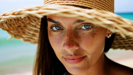 Close-up video of a woman in a straw hat at the beach, showcasing her eyes and freckles