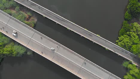 top-down aerial shot of vehicles moving along with the two bridges connecting two sides of the land been separated by a river shot with a drone in 4k