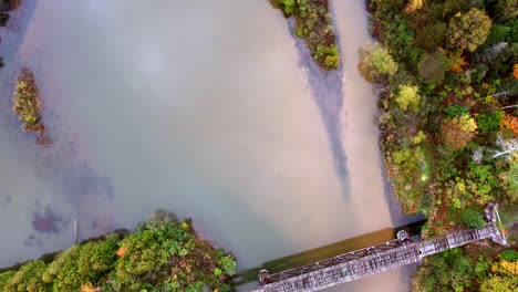 Straight-down-time-lapse-over-a-river-in-Northern-Michigan-during-early-autumn-showcasing-foliage-and-decrepit-bridge-and-river-during-season-change