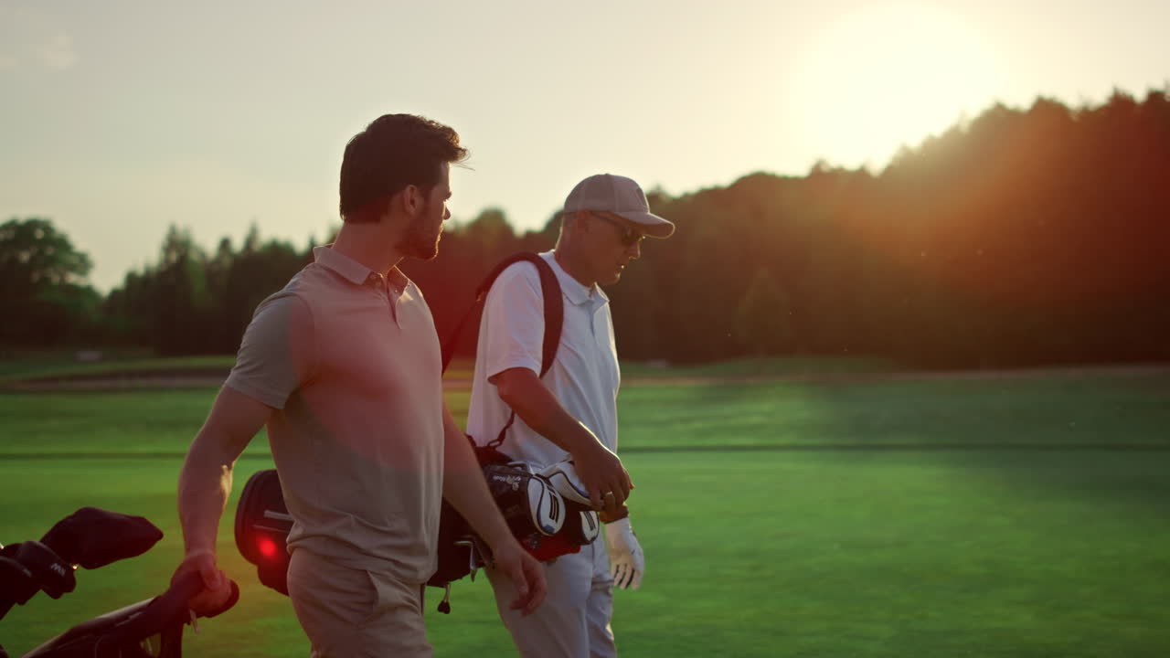 Businessmen walking golf course outside. Two players carry clubs in sportswear.