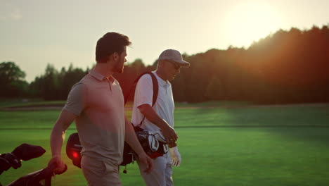 Businessmen-walking-golf-course-outside.-Two-players-carry-clubs-in-sportswear.