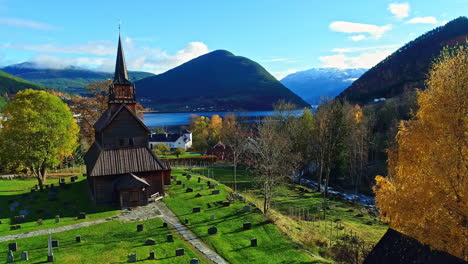 Aerial-drone-forward-moving-shot-of-a-church-and-graveyard-in-Norway-with-the-view-of-beautiful-mountain-range-in-the-background-at-daytime