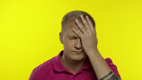 Portrait-of-young-caucasian-man-posing-in-pink-t-shirt.-Dissatisfied-guy-puts-hand-on-face,-facepalm
