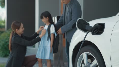 progressive young parents and daughter living in a home with an electric car.