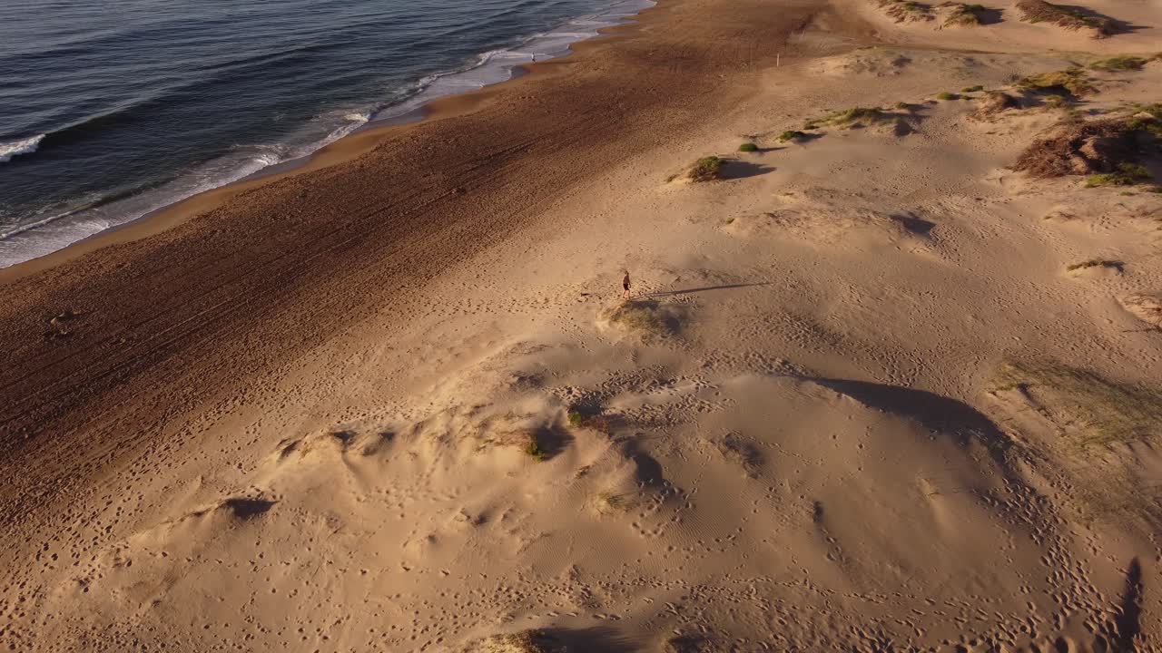 toma aérea de un hombre haciendo ejercicio físico en las dunas de arena en la playa durante la puesta de sol
