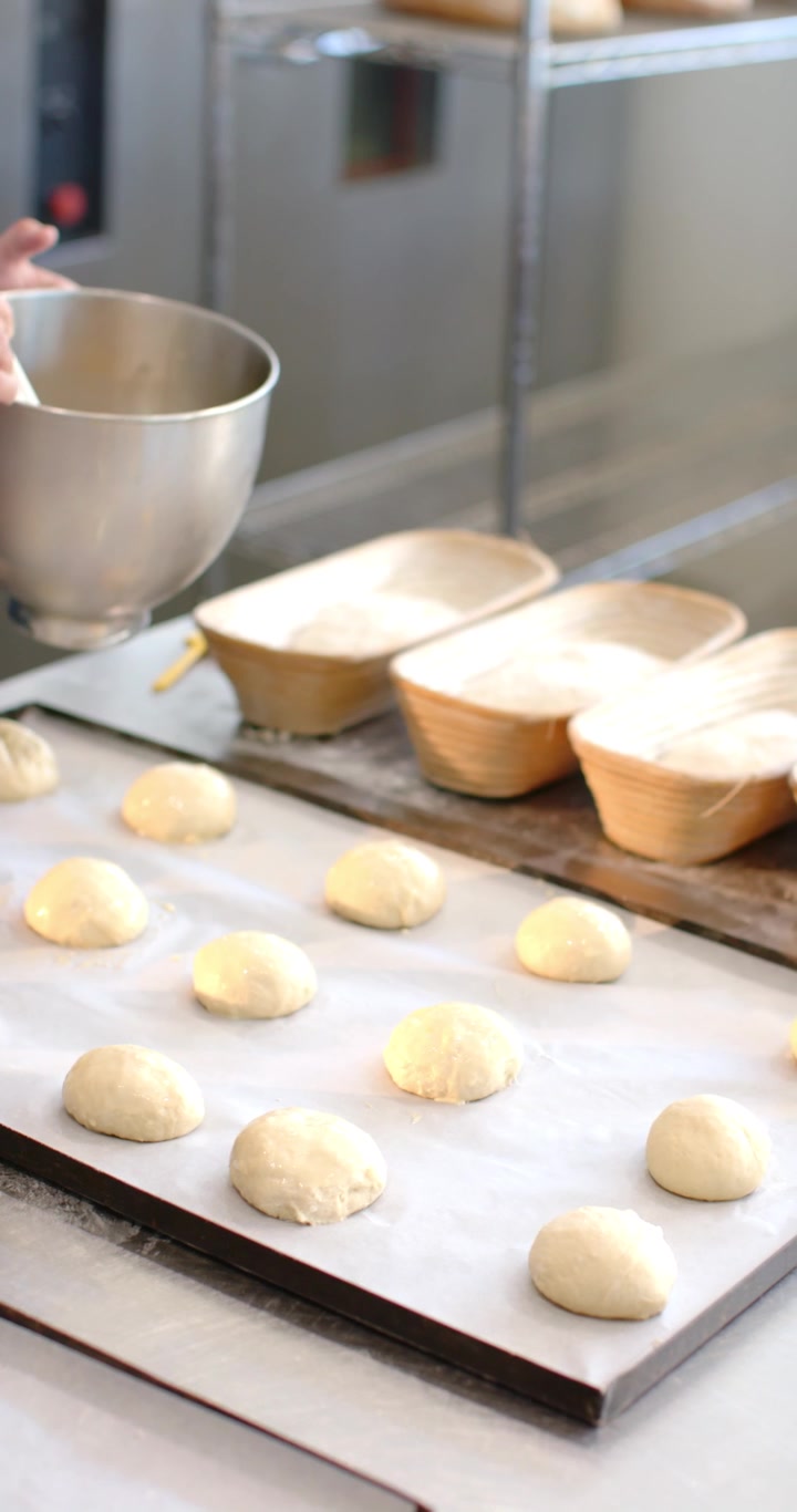Dipping brush in bowl African American woman coating dough rounds for baking at counter, copy space