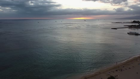 4K-cinematic-crane-shot-from-behind-a-palm-tree-at-Waikiki-Beach-during-sunset-in-Oahu