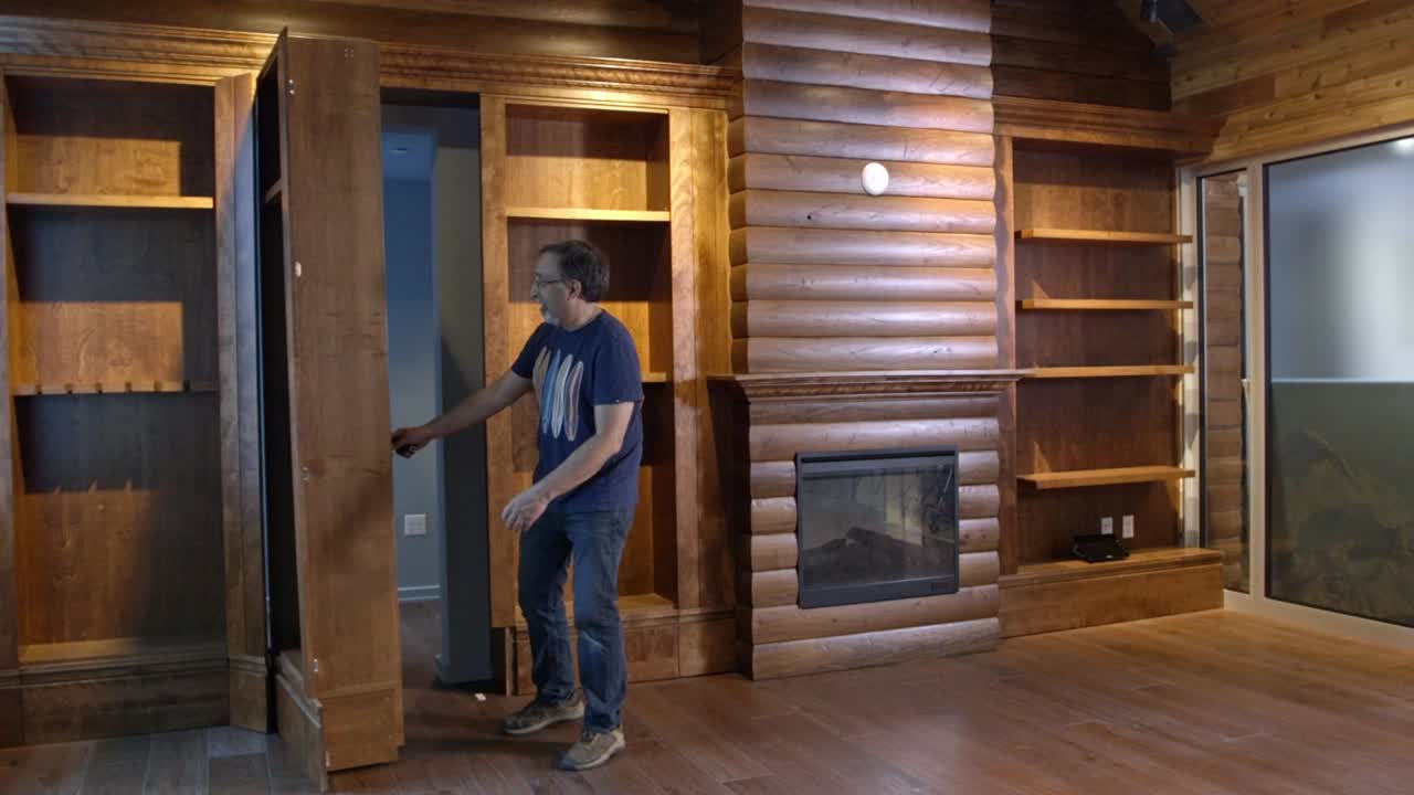 A hidden doorway in a wall of bookshelves opens to reveal a concealed room. From within a man comes out examining the door with great interest and wonderment