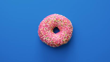 anillo apetitoso rosquilla cubriendo el glaseado rosa girando lentamente aislado azul. disparado con cámara roja en 4k