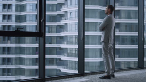 Hombre-Exitoso-Cruzando-Las-Manos-Mirando-La-Ventana-En-El-Centro-Del-Edificio-De-Oficinas-De-Negocios.