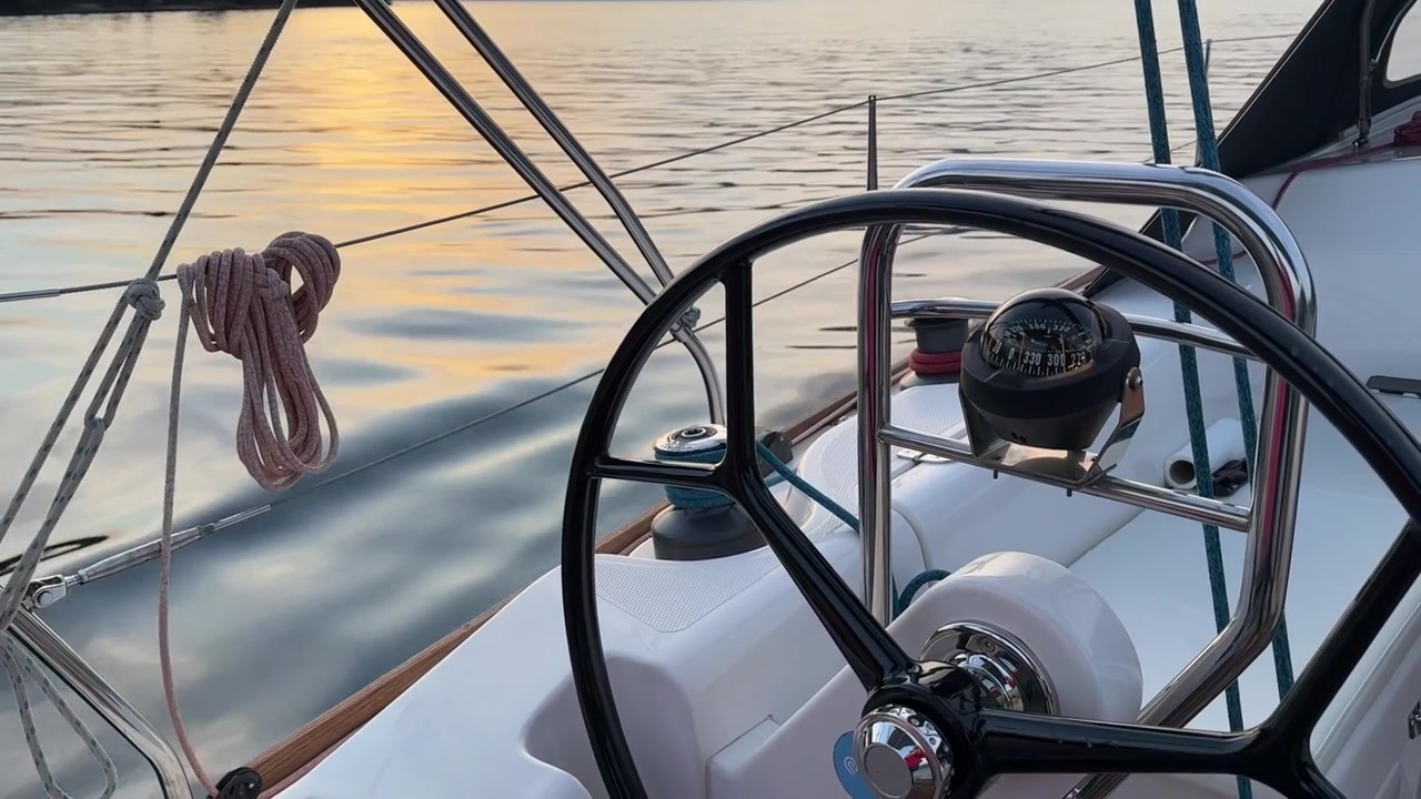 Un primo piano del timone e della bussola di una barca a vela mentre scivola su acqua calma durante un tramonto all'ora d'oro in Montenegro