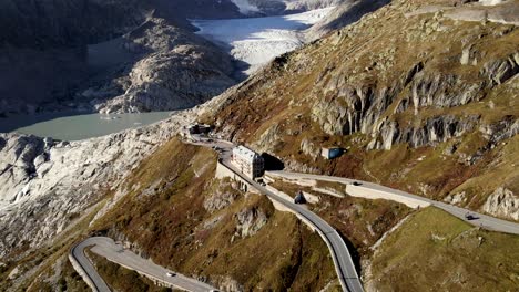 Sobrevuelo-Aéreo-Sobre-El-Paso-De-Montaña-De-Furka-En-La-Frontera-De-Valais-Y-Uri-En-Suiza-Con-Una-Vista-Panorámica-Desde-El-Glaciar-Del-Ródano-Hasta-Los-Autos-Que-Conducen-Por-Las-Numerosas-Curvas-De-La-Carretera