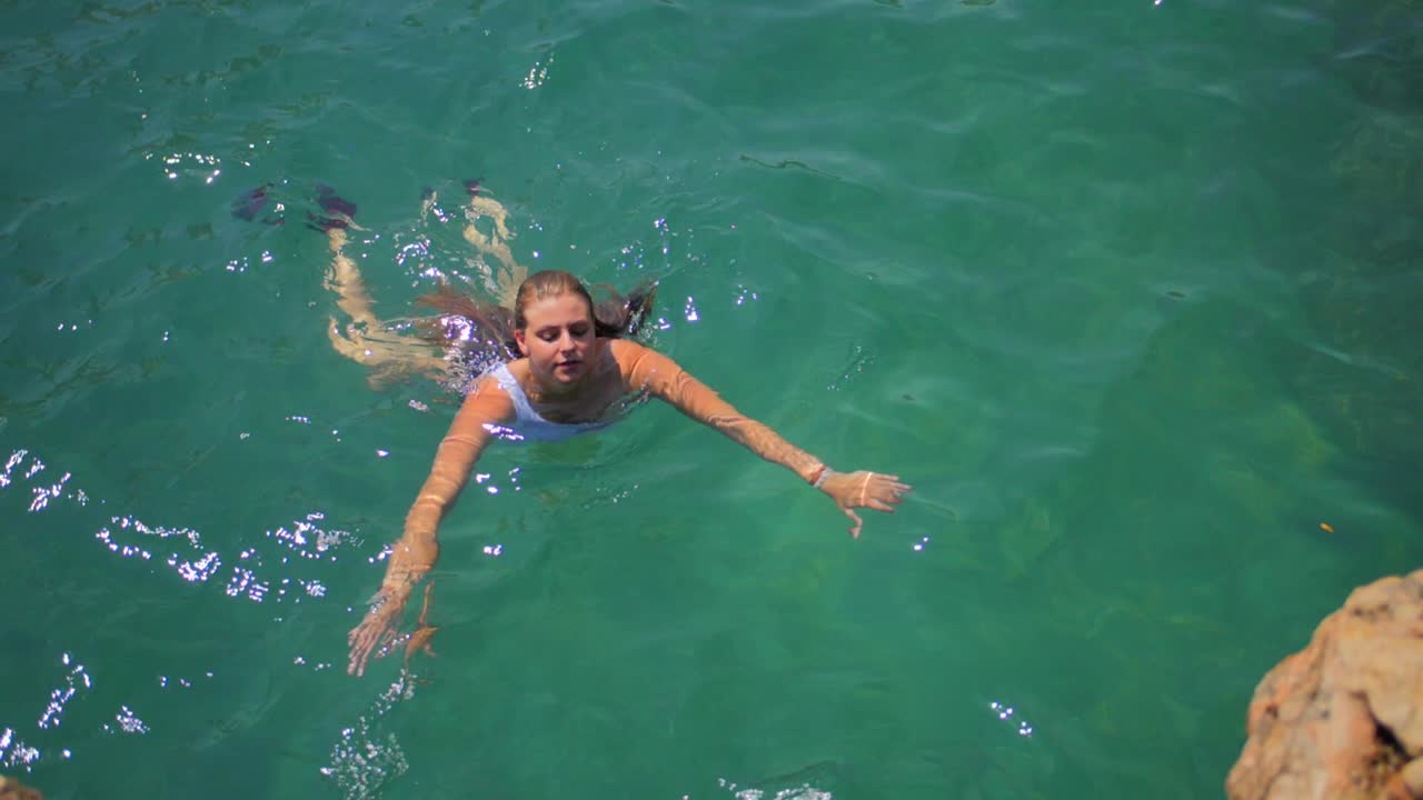 Donna in bikini che nuota vicino a una costa rocciosa e un mare cristallino