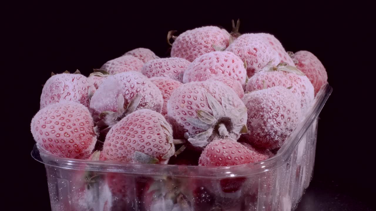fresas fresas de fresa congeladas en paquetes de alimentos de plástico desechables sobre un fondo negro. rotación de 360 grados, primer plano