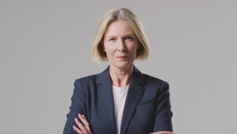 studio portrait of serious mature businesswoman folding arms against plain background