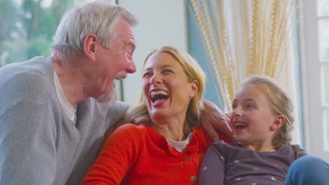 loving grandparents hugging granddaughter sitting on sofa at home together