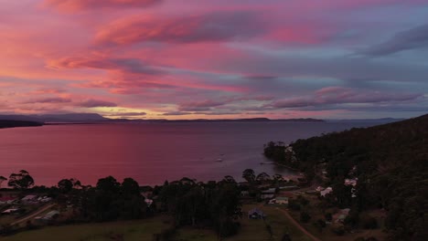 dron aéreo lento pan alrededor de la impresionante playa púrpura de la isla de la puesta del sol al atardecer, cielo púrpura y naranja y cordillera con pequeñas chozas y bosque