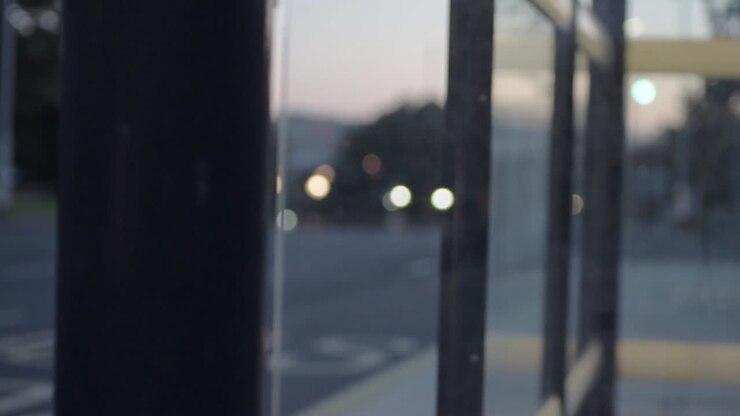 Luci sfocate di veicoli urbani al crepuscolo attraverso i finestrini di una fermata dell'autobus.