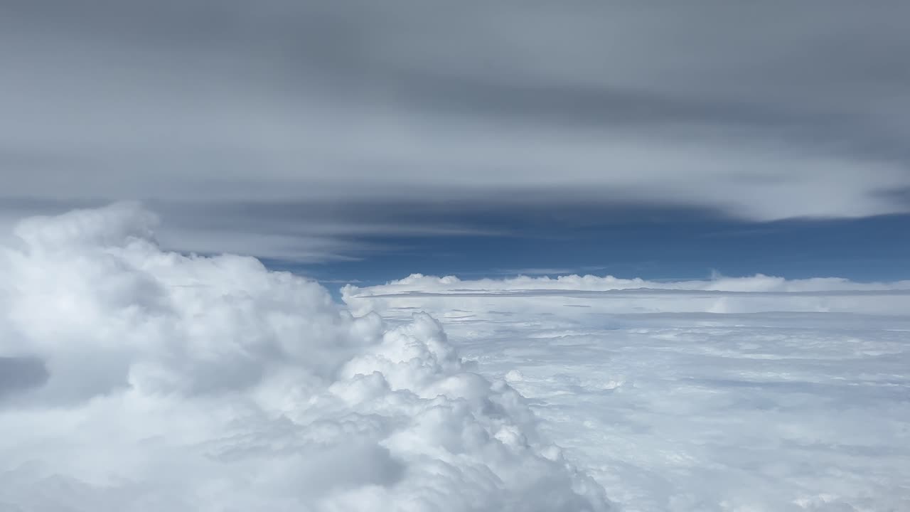 A serene aerial view of moving clouds and open sky captured from an airplane window. Soft cloud layers drift smoothly beneath the aircraft, creating a peaceful and cinematic travel atmosphere