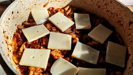 pot of spicy meat stew topped with sliced cheese melting into rich sauce