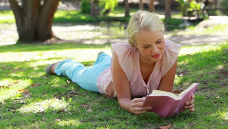 a woman lying down reading a book in the park as she then looks at the camera