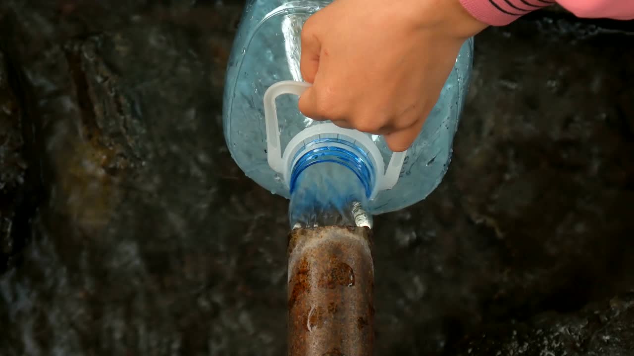 el hombre vierte con la mano agua de manantial natural en la botella.