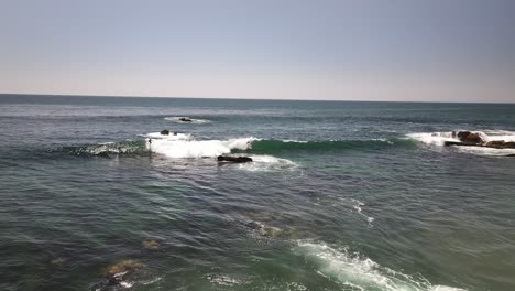 Surfers-in-Laguna-Beach-California-riding-a-wave-in-the-Pacific-Ocean,-aerial-drone-view-flying-towards-the-waves