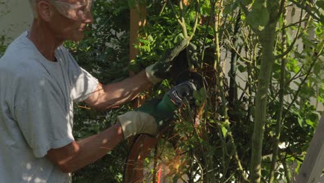 mature man grinding metal structure in garden wearing protection during summer day, handheld medium shot