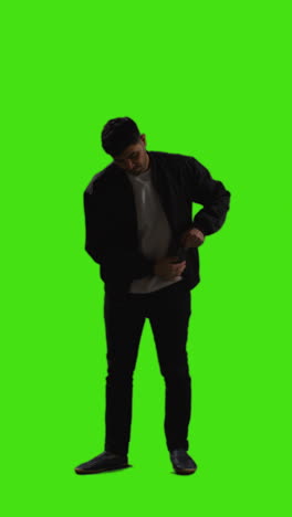 Vertical-Video-Full-Length-Shot-Of-Young-Man-Answering-Call-On-Mobile-Phone-Standing-Against-Green-Screen-With-Low-Key-Lighting-1