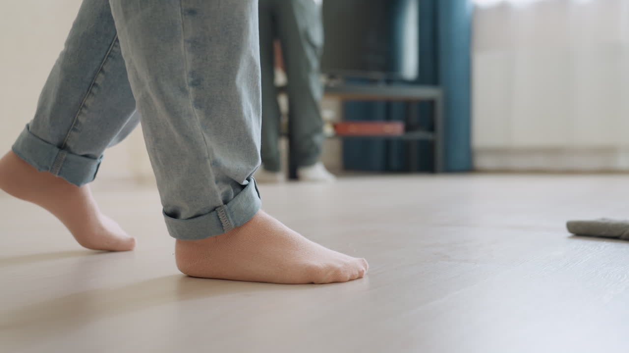 Close up of barefoot woman mopping floor while son cleans television in bright living room, teamwork highlights family cooperation and care for maintaining clean household environment