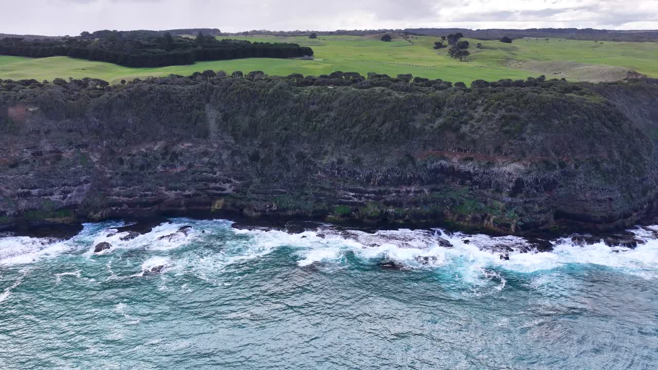 Drone captures rugged coastline, ocean waves, and dramatic cliffs under overcast daylight at Cape Schanck