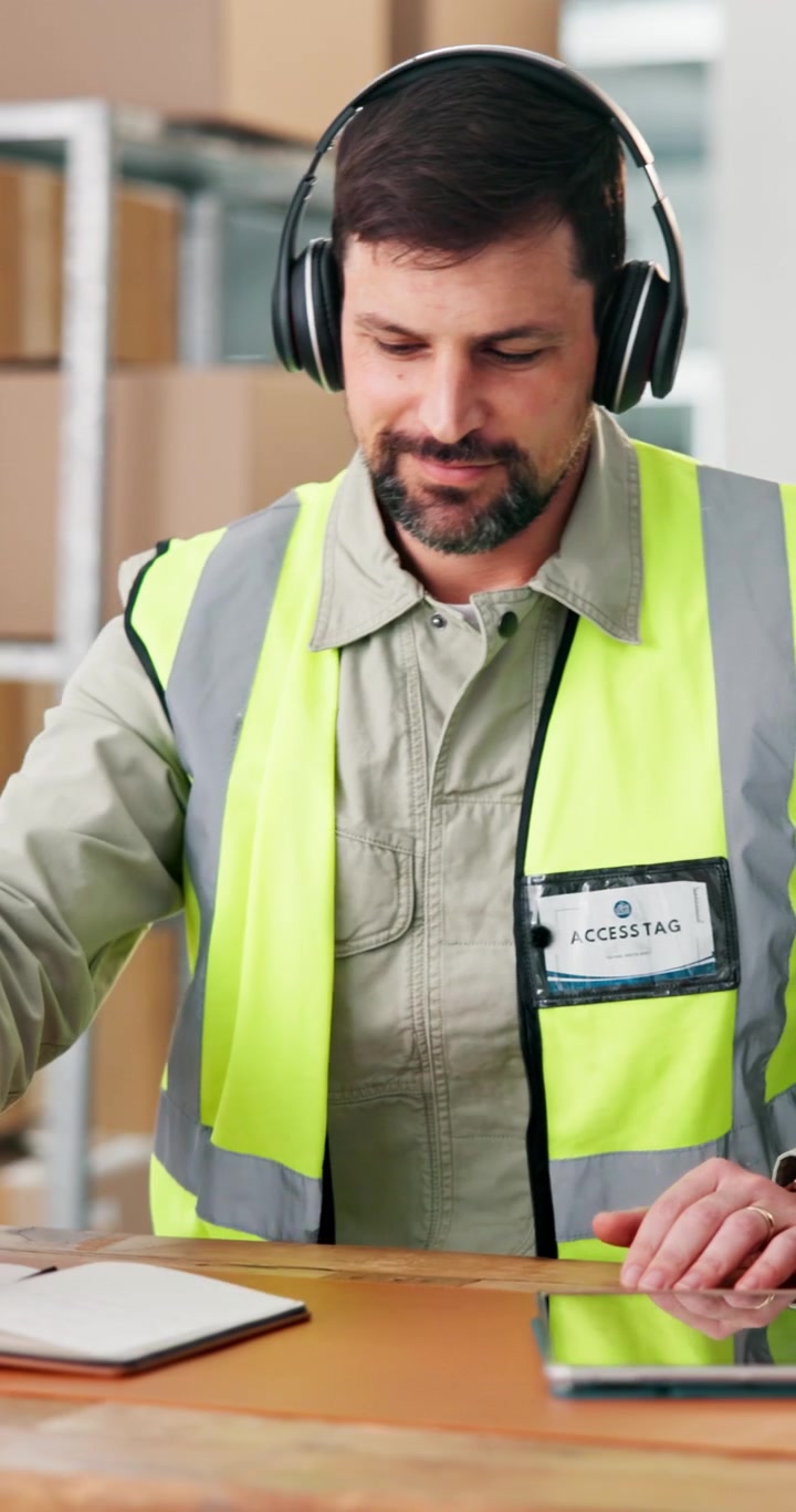 Warehouse Worker Using Smartphone and Writing in Notebook