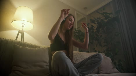 mujer con auriculares escuchando música en el teléfono inteligente y moviendo su cuerpo en la postura del loto en el suelo de la sala de estar