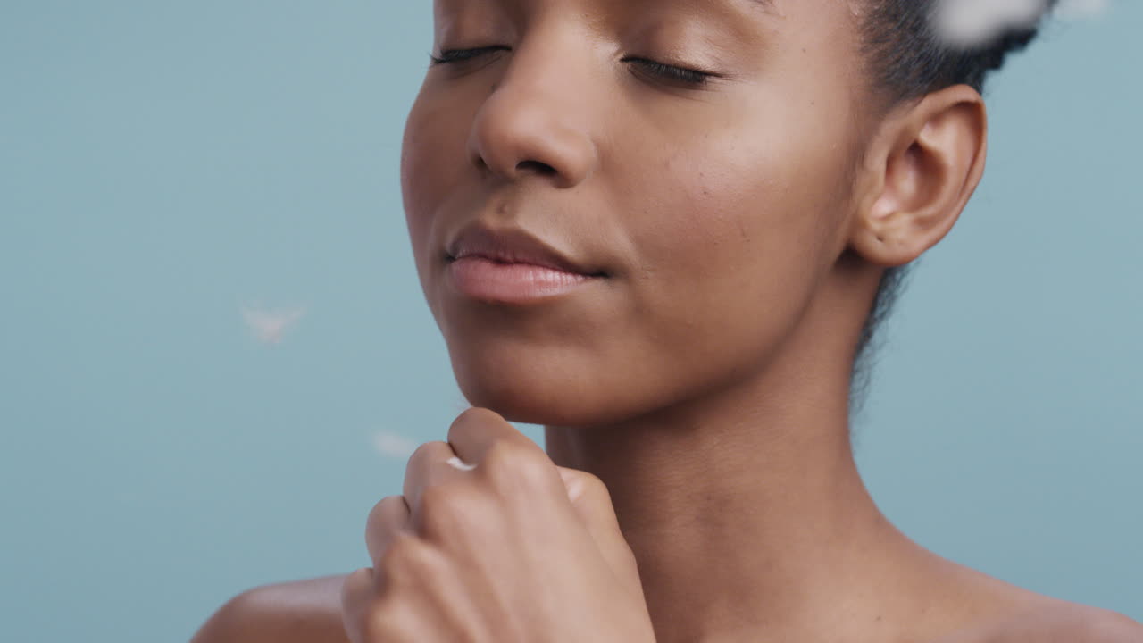 close up beauty portrait beautiful african american woman touching face with feathers falling on soft skin enjoying sensual skincare gently caressing healthy complexion in slow motion
