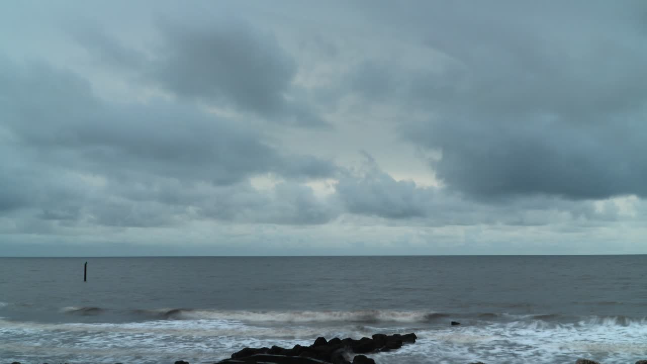 Storm Clouds Moving In As Tide Washes Against The Shore On Grey Day At English Seaside Location. One Second Exposure Time Lapse