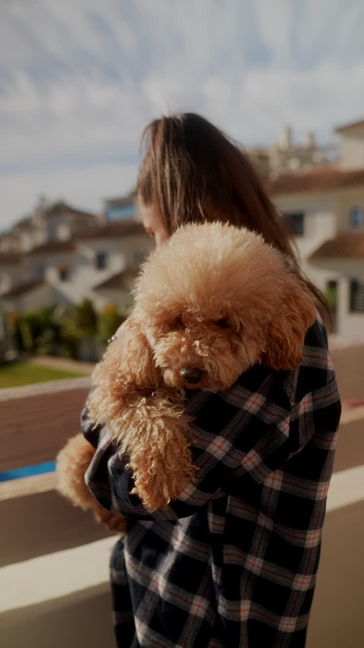 mujer sosteniendo un caniche peludo en un balcón