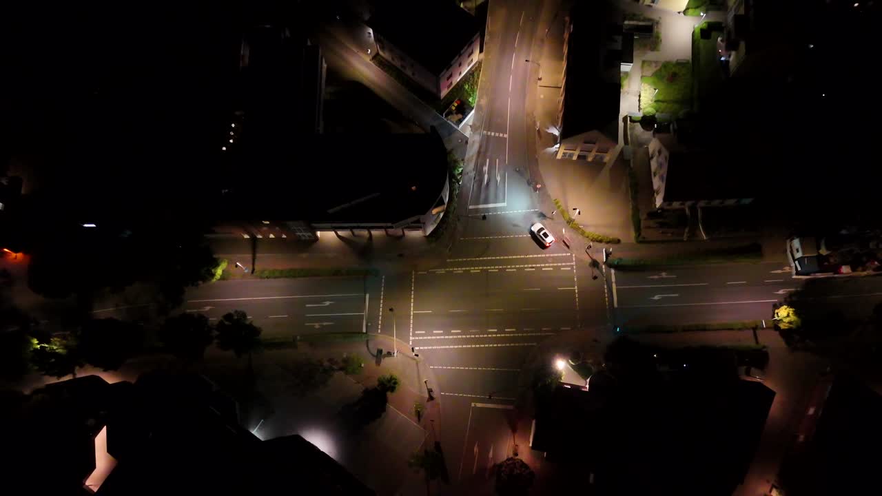 Car on junction turning into lighting street of small american town at night. Houses and homes in suburb area of USA. Aerial top down rising shot. Summer night in USA