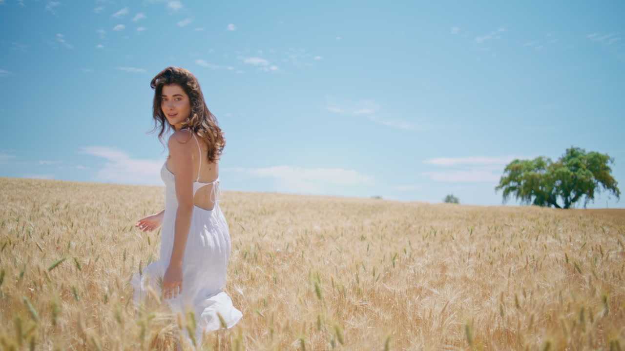 mujer despreocupada caminando cultivos dorados vista trasera. feliz mujer joven mirando cámara