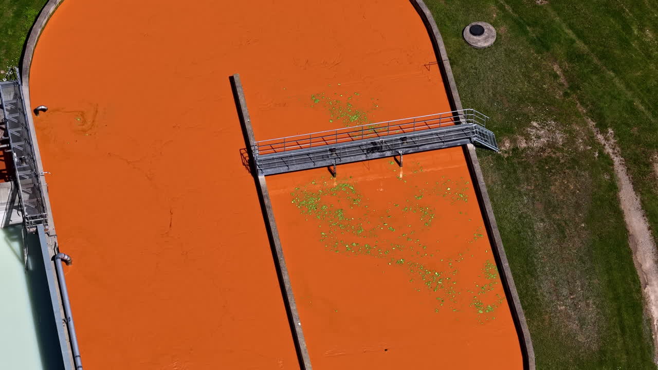 Orange wastewater swirls in treatment tank, aerial flyover of industrial sanitation