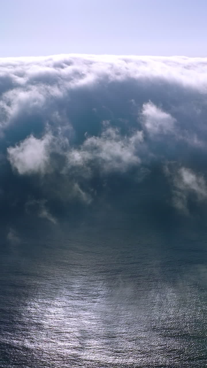 Thick white fog spreading to the coastline from water. Amazing cloudscape of haze on sunny summer day. Aerial view. Vertical video