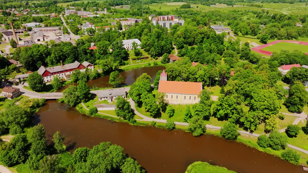 Cinematic aerial of Aizpute town highlighting bridge, river and historic church