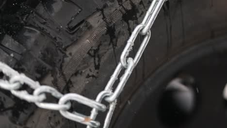 snow chains wrapped tightly around a jeep off road tire while it flurries