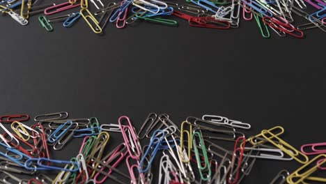 close up of scattered colourful paper clips with copy space on black background, in slow motion