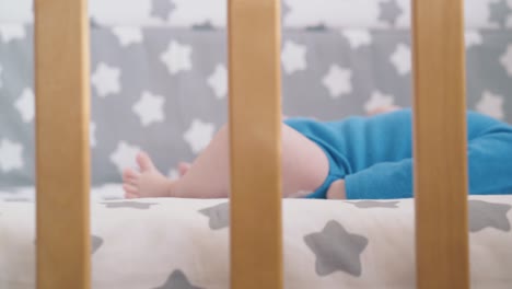 funny newborn kid bothers hands lying in baby bed in room