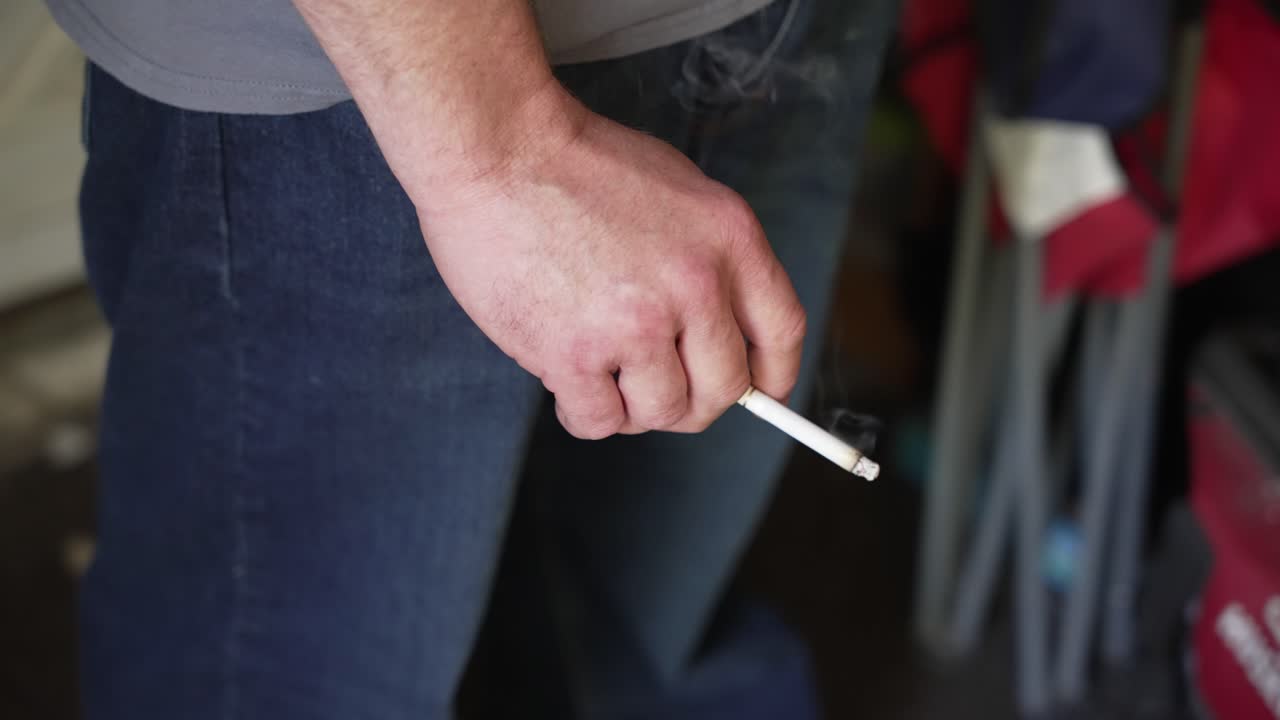 Close-up of a caucasian male hand holding a cigarette as it burns.