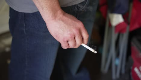 close-up of a caucasian male hand holding a cigarette as it burns.