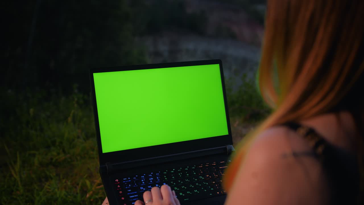 una joven trabaja en una computadora portátil con una pantalla verde en la cima de una montaña.