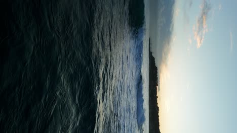 Vertical-format-of-surfers-riding-waves-at-sunset-along-Varazze-coastline-in-Luguria,-Italy